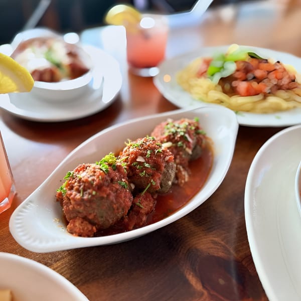 Petrini's Italian meatballs in red sauce with parsley, pasta, and drinks on a wooden table.