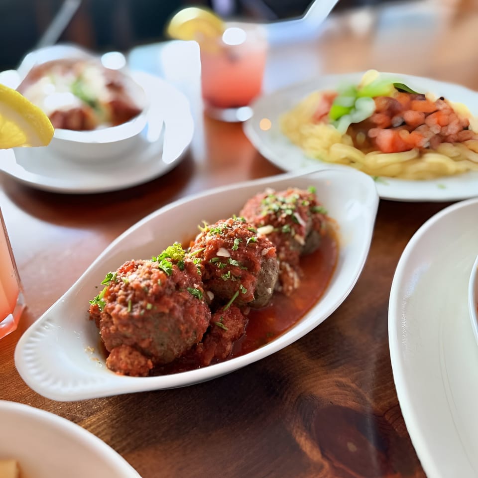 Petrini's Italian meatballs in red sauce with parsley, pasta, and drinks on a wooden table.