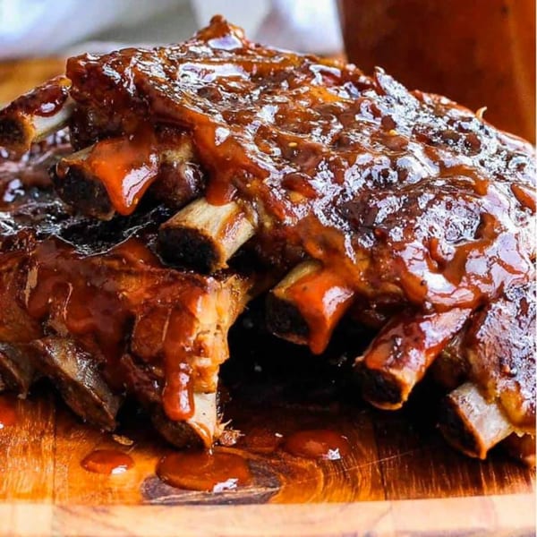 Close-up of Petrini's San Diego's BBQ ribs, glistening with sauce on a wooden board.