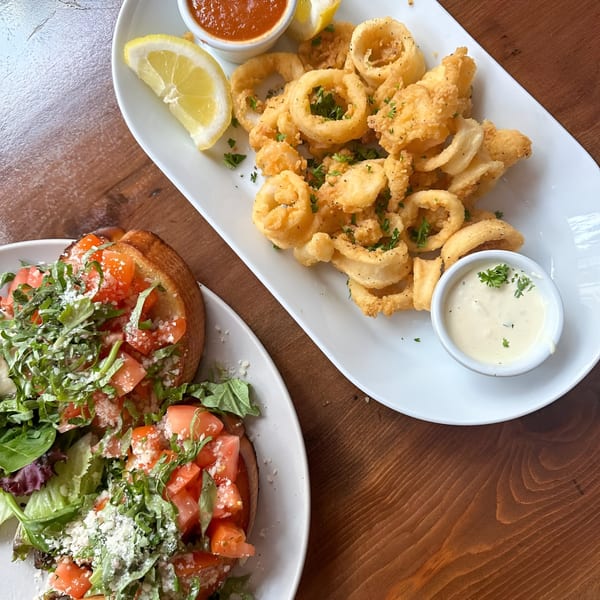 Plates of golden fried calamari with lemon and dipping sauces, and bruschetta with tomatoes and greens.