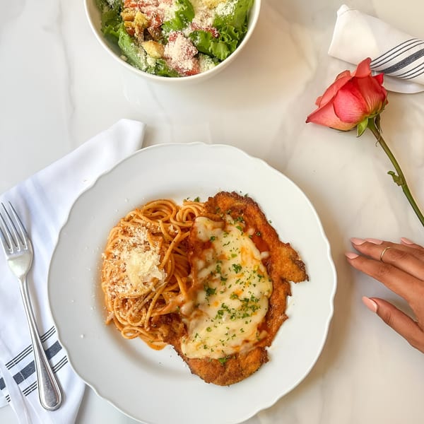 Chicken parmesan with spaghetti and a side salad, with a pink rose and a hand reaching for it.