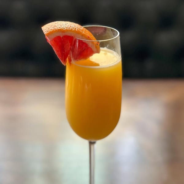 A mimosa cocktail in a champagne flute, garnished with a slice of grapefruit.