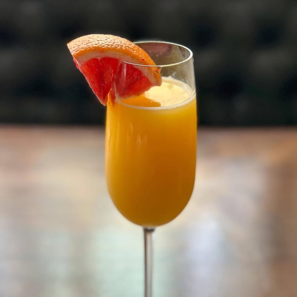 A mimosa cocktail in a champagne flute, garnished with a slice of grapefruit.